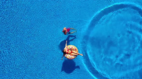 Aerial View of Man Dives Into the the Pool While Girl Is Lying on a Donut Pool Float alt