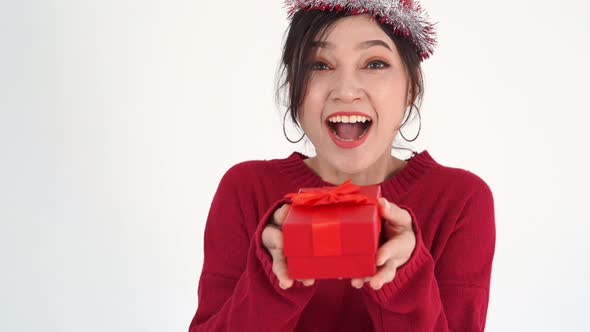 cheerful young woman with hat and holding a red christmas gift box in a gesture of giving