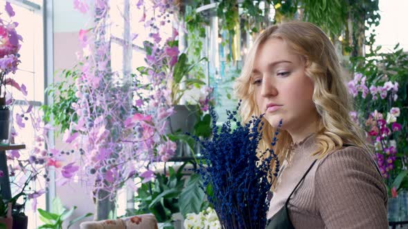 A Young Woman is Attentively Examining a Bouquet of Blue Flowers Placed in a Blue Transparent Vase alt