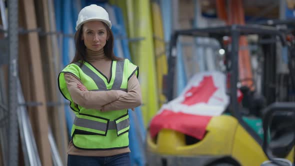 Serious Woman Crossing Hands Looking at Camera with Canadian Flag on Forklift at Background alt