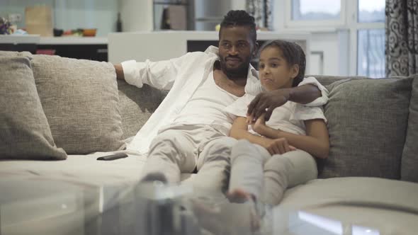 Wide Shot Carefree Relaxed African American Man Girl Watching TV Evening Home alt