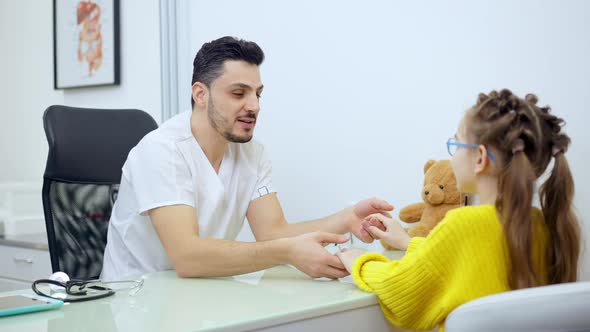 Middle Shot of Joyful Male Pediatrician Holding Hands of Patient Talking and Smiling alt