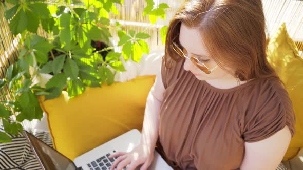 Girl in Brown Blouse and Sunglasses Works on Laptop Closeup