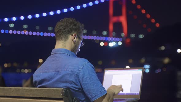Man doing work on laptop against night sea view. alt