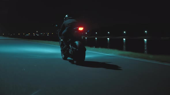 A Man Rides a Sports Motorcycle Through the City at Night Against the Backdrop of the River alt