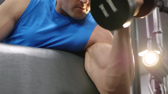 Man Performs an Exercise with Dumbbells on a Simulator in the Gym alt