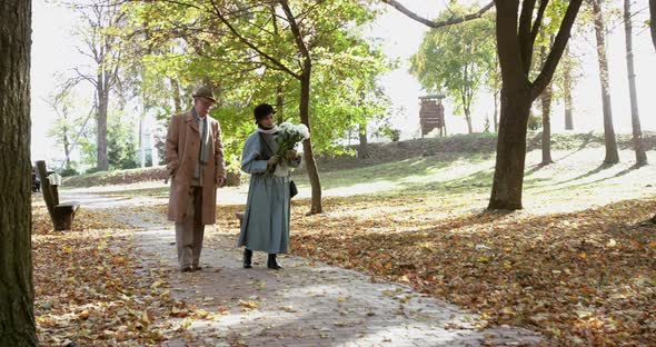 Elderly Lovely Married Couple with Bouquet of Flowers Walking in Autumn Park alt