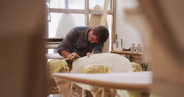 Caucasian male surfboard maker working in his studio and making a wooden surfboard alt