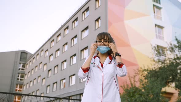 Young Female Intern or Medical Student Taking Off Surgical Face Mask and Looking at Camera alt