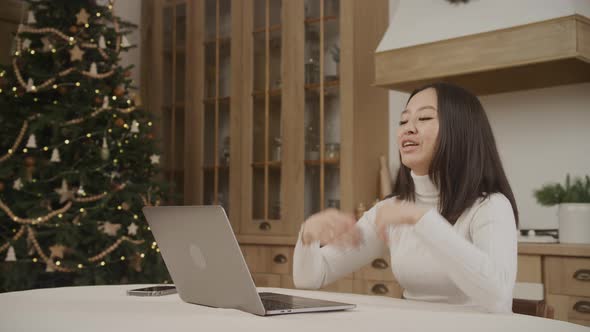 Young Adult Asian Woman on a Video Call on Her Laptop with a Christmass Tree on Background Indoors alt