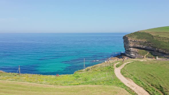 Tourists walking in border of green blue turquoise seaside cliff. Aerial alt