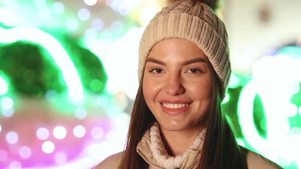 Face Young Woman in Hat Looking at Camera Smiling Around Christmas Lights in City Center 