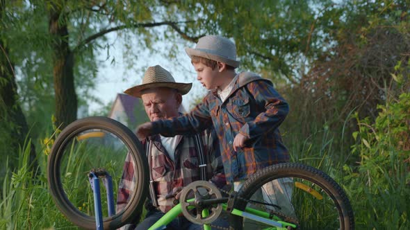 Cheerful Happy Grandfather and Grandson in Hats Spin a Bicycle Wheel During a Family Weekend alt