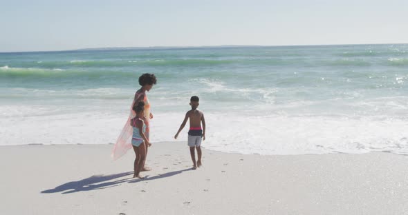 Smiling african american mother with children wearing swimming suits on sunny beach alt