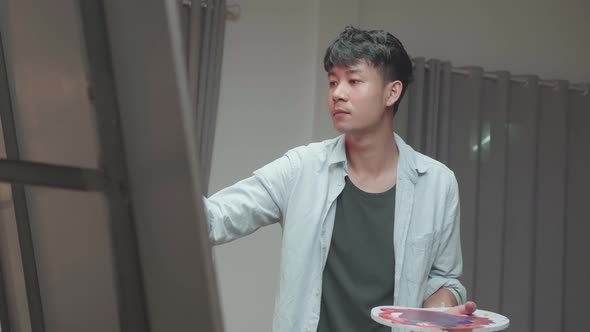 Asian Male Artist Painting And Looking At His Picture alt