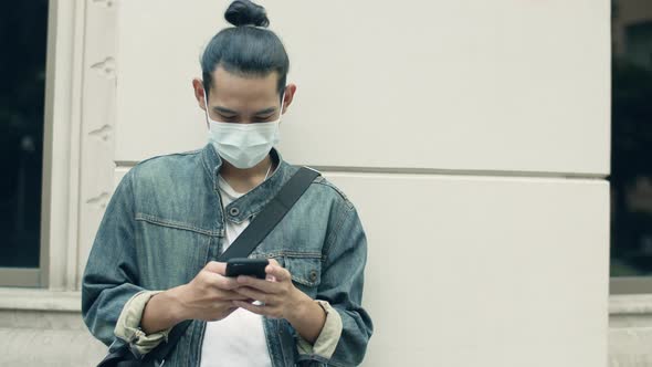 Asian man wearing a surgical mask and using smartphone.