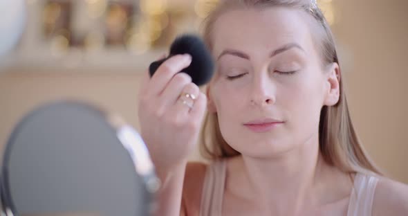 Young Woman Doing Makeup in Front of Mirror at Home alt