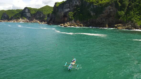 Indonesian fishermen in small fishing boat on turquoise ocean by Kesirat cliffs alt