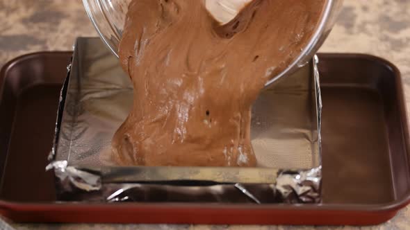 A Chef in the Kitchen Pouring Chocolate Cake Batter Into a Square Baking Pan To Go in the Oven for