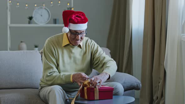 Excited Elderly Man in Santa Hat Opens Box Say Wow Show Two Thumb Up Rejoices in Unexpected Gift alt
