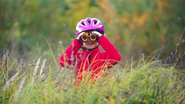 A little girl in a protective helmet in nature looking through binoculars where to go.