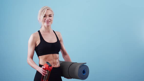 Happy sports woman smiling holds a fitness mat and a bottle of water. Concept of fitness and sports alt