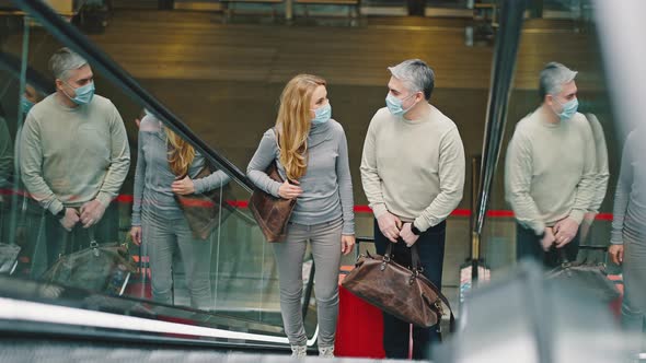 Happy Man and Woman Wearing Protective Medical Masks Riding Up on Escalator at Airport Building with alt