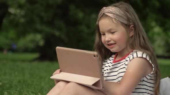 Funny Girl 67 Years Old Sits on the Grass in a Summer Park with a Tablet alt