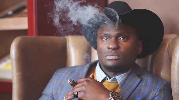 Young black man wearing suit and hat gangster style smoking cigar. alt