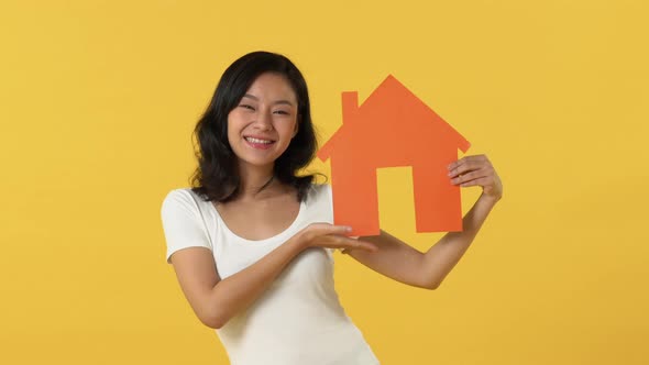 Happy smiling young Asian woman displaying the cut out orange house model