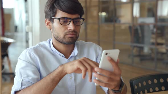 Smiling Indian Business Man Using Cellphone Apps Working in Office alt