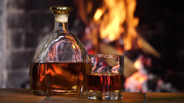 Bottle and Glass with Whiskey or Cognac on the Background of Fire in the Fireplace alt
