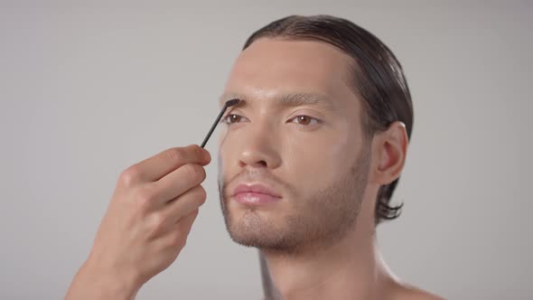 Unrecognizable Make-Up Artist Combing Eyebrows of Handsome Man alt