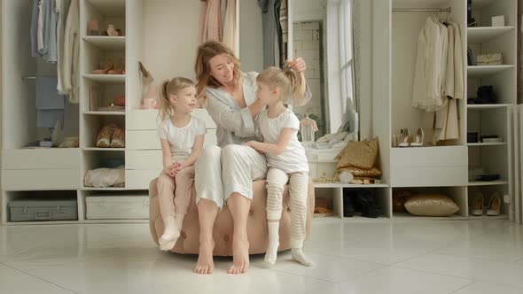Mom and Twin Daughters in Blue Pajamas Sit in Front of the Closet at Home