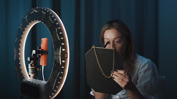 Female Fashion Blogger Applies Makeup Using Brush Holding Mirror in Hands