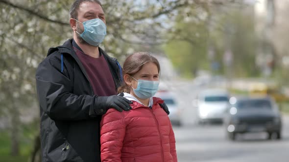 A bearded dad adjusts his daughter's medical mask on the street of a European city 