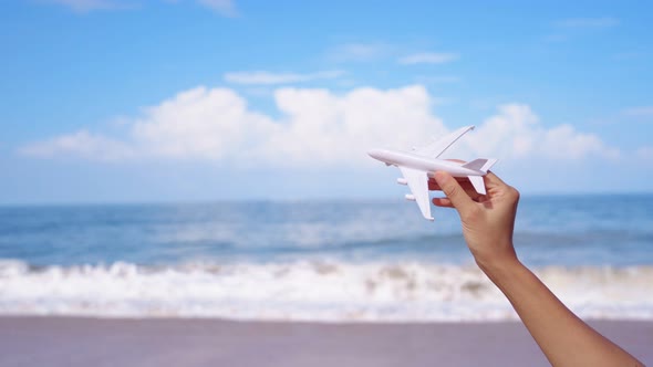 Hand holding a miniature airplane at the tropical beach on a sunny day