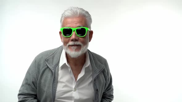 Stylish Emotional Old Man Pensioner with a Gray Beard in Green Glasses Dances with Funny Emotions on