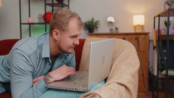 Adult Man Using Laptop Computer Lying on Sofa at Home Working Online Shopping Watching Movies alt