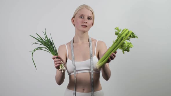 A Slender Woman with a Measuring Tape Around Her Neck Holds Green Onions and Celery in Her Hands