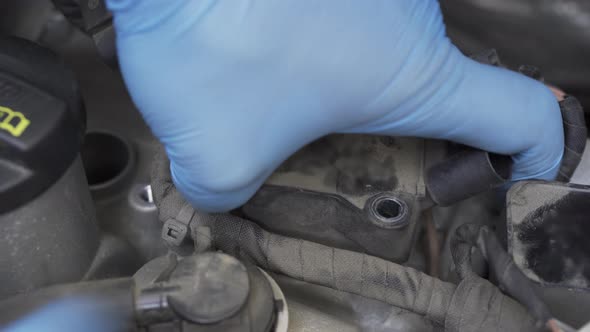 Hands in Protective Gloves Taking Out Ignition Coils in Car Engine Bay