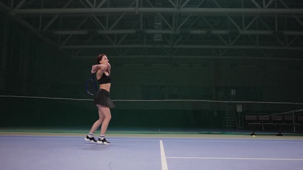 Tennis Training or Game on Indoor Court Young Woman is Striking Ball By Tennis Racquet Fulllength alt