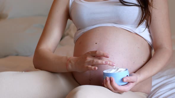 Pregnant woman rubbing moisturizer into her belly, taking care of her skin during pregnancy