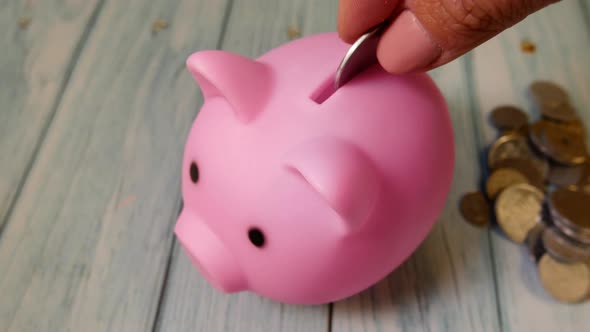 Unrecognizable Hand Puts Coins in a Piggy Bank in the Form of a Pink Pig
