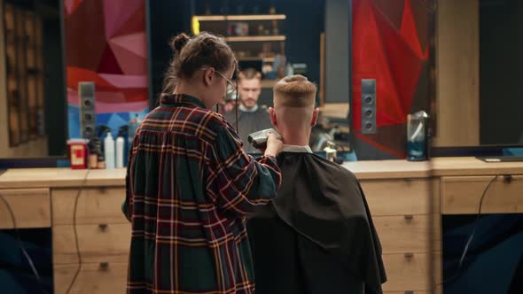 Barbershop: woman hairdresser cuts man's hair with a razor alt