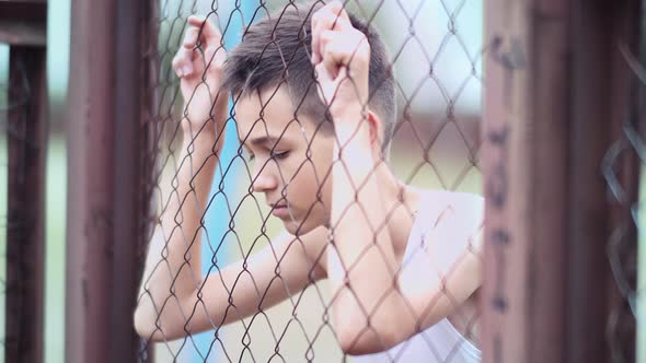 Refugee Sad Boy Stands Alone Head Bowed Near the Fence Frustrated Boy Dropped Eyes Cinematic Shot