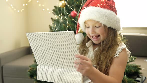 Happy Little Girl in Santa Hat on the Background of the Christmas Tree. The Child Is Happy  alt
