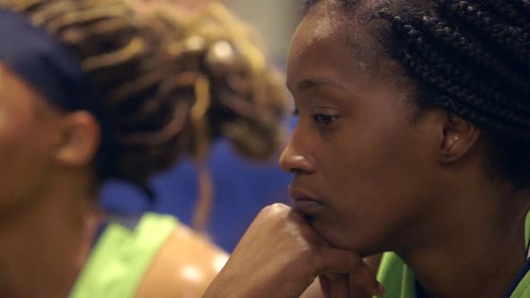 An African American female basketball player listens to a pep talk in the locker room between halves alt