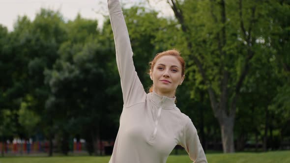 Caucasian young woman doing torso, arms, legs strech in the park. alt