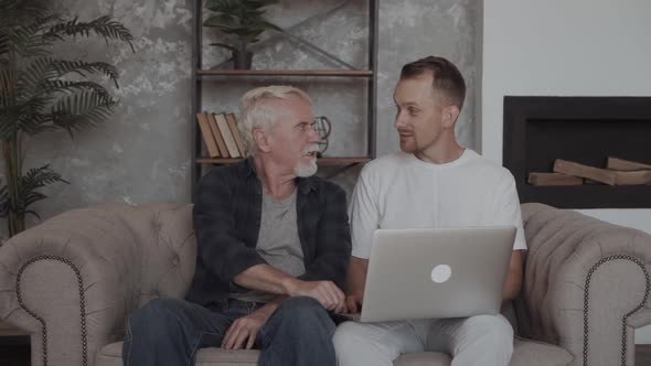 Grandson \ Son Helping Grandfather To Use the Internet and Online Services on Laptop At Home alt